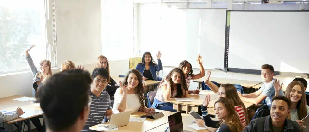 Rear View Of Male High School Teacher Standing At Front Of Class Teaching English for Exams Lesson