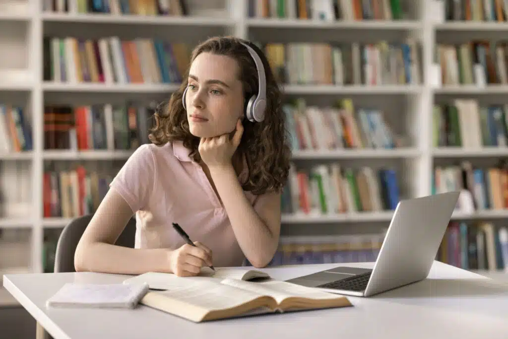 Student listening to headphones while studying with laptop and books