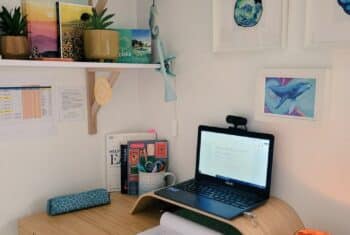Lucy's online classroom set-up: a desk with laptop, bookshelf and wall decor